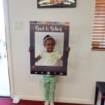Young girl smiling and holding a “Back to School” photo frame at a community event.
