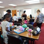 Children and families selecting toys and school supplies from tables during a community giveaway event.