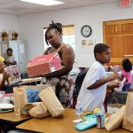 Families browse and collect shoes, toys, and supplies during a back-to-school giveaway event inside a community center.